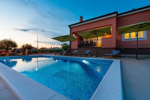 A swimming pool with lounge chairs and umbrellas, a building with a balcony, and a clear sky. - Villa Solis Zadarvillas (Zadar)