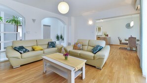 Ein geräumiges Wohnzimmer mit zwei beigen Sofas, einem Holztisch und einem Essbereich mit Tisch und Stühlen.