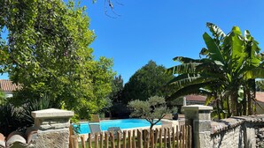 A swimming pool surrounded by a stone wall and wooden fence, with lush greenery and trees in the background. - Glamping TENTE LODGE SAFARI DE LUXE, vue sur le coteau et vignes (Chadenac)