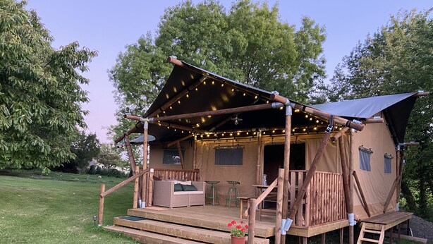 A rustic wooden cabin with a deck, string lights, and a small garden. - Glamping TENTE LODGE SAFARI DE LUXE, vue sur le coteau et vignes (Chadenac)