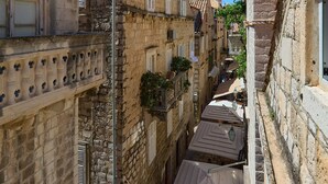 Un carrer estret amb edificis de pedra, una petita zona de seients a l'aire lliure i una persona caminant.