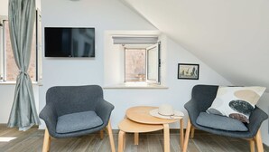 Habitació moderna amb dos butaques grises, una taula de fusta petita i un televisor fixat a la paret.