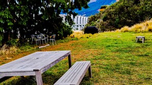 Et picnicbord i en græsplæne med stole og en genstand under et tag i baggrunden.