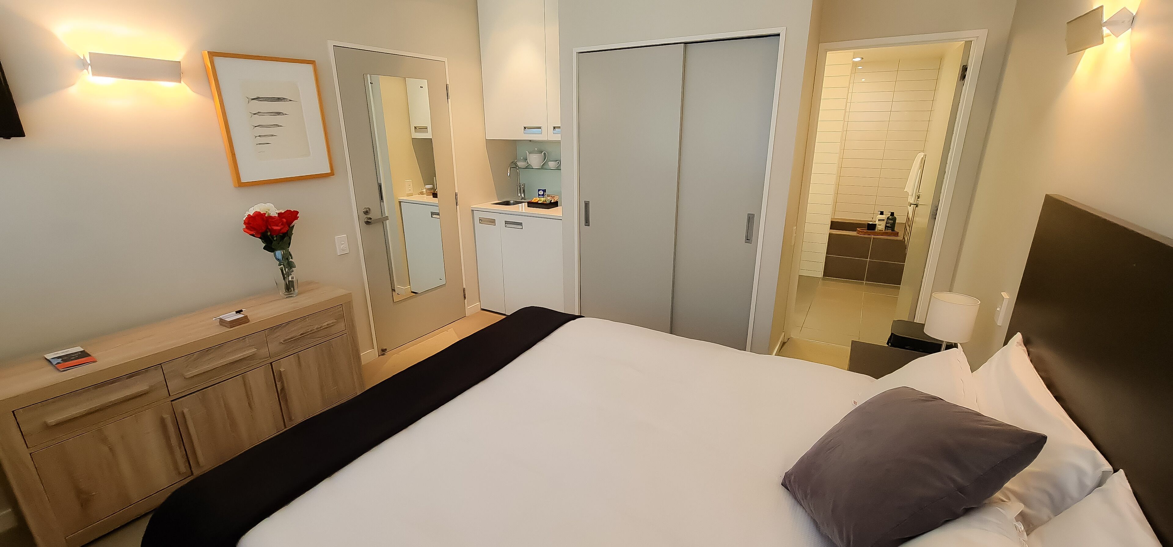 Ein Hotelzimmer mit Bett, Schminktisch, Spiegel, Kleiderschrank und einem durchgegangenen Tür sichtbaren Badezimmer.