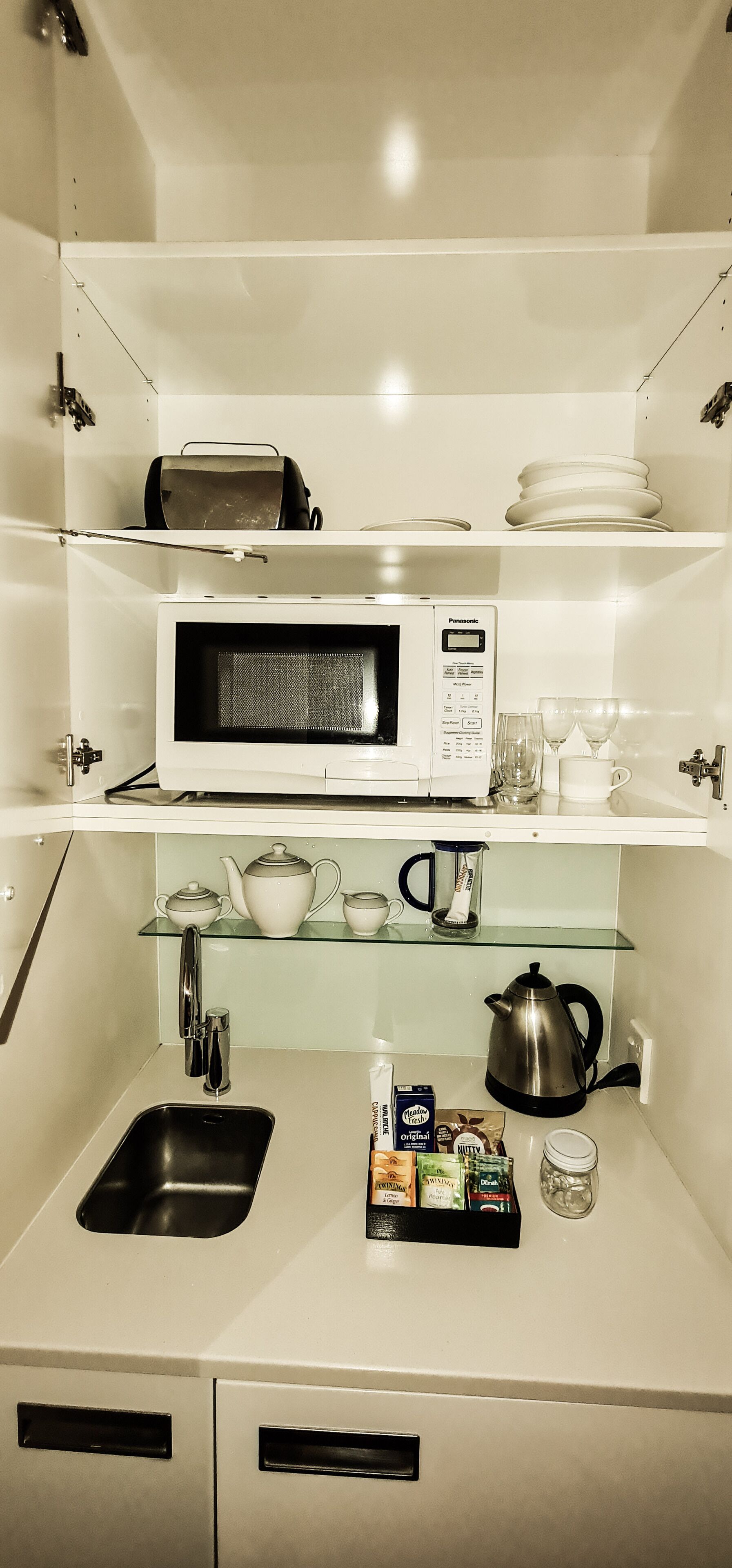 A kitchenette with a microwave, tea set, and a coffee maker.