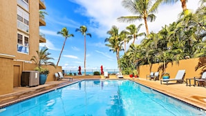 A swimming pool with lounge chairs and palm trees, surrounded by a building with balconies.