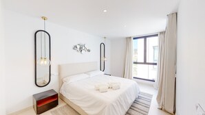 Un dormitorio moderno con una cama grande, dos espejos en la pared, una mesita de noche y una ventana con cortinas.