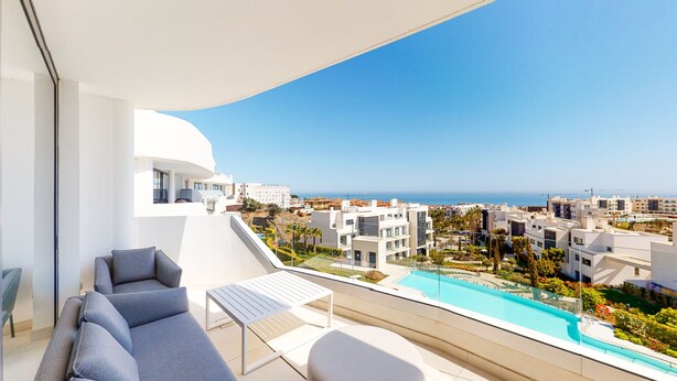 Un balcón con piscina, mobiliario moderno y vista al mar y edificios circundantes.