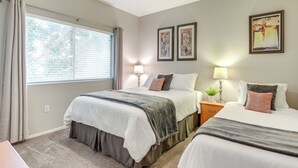 A bedroom with two beds, a ceiling fan, a window with curtains, and two wall-mounted lamps.