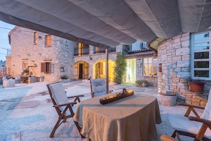 An outdoor patio area with stone walls, a table with a tablecloth, and several chairs.