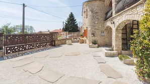 A courtyard with stone flooring, a stone building with arched windows, and a metal fence. - Apartment Alba (Kastelir-Labinci)