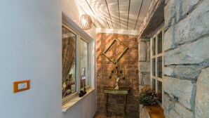 A narrow hallway with a stone wall, a window with a curtain, and a small table with a vase of flowers. - Apartment Alba (Kastelir-Labinci)