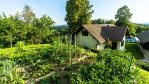 Een klein huis met schuin dak, omgeven door een verzorgde tuin met diverse planten en een helder uitzicht over het landschap.