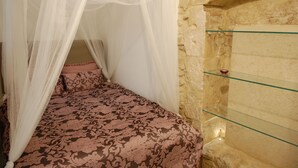 A room with a bed under a canopy, a stone wall, and a glass shelf with a small item on it. - 2 BR apt., gated courtyard, right by ocean & sites (Siracusa)