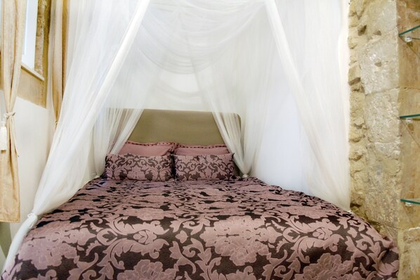 A bed with a canopy, patterned bedding, and a stone wall. - 2 BR apt., gated courtyard, right by ocean & sites (Siracusa)