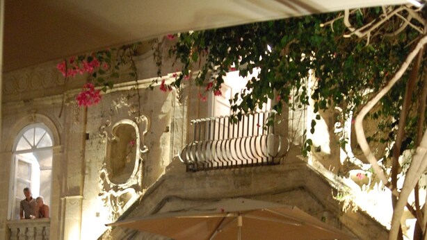 An outdoor dining area with ornate metal chairs and tables, a decorative archway, and a balcony with a railing. - 2 BR apt., gated courtyard, right by ocean & sites (Siracusa)