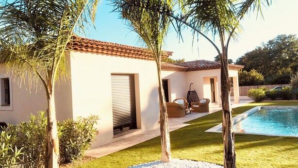 Een huis met een zwembad, tuinmeubilair en palmbomen.
