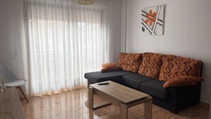 En stue med sofa, sofabord, stol og et maleri på væggen.