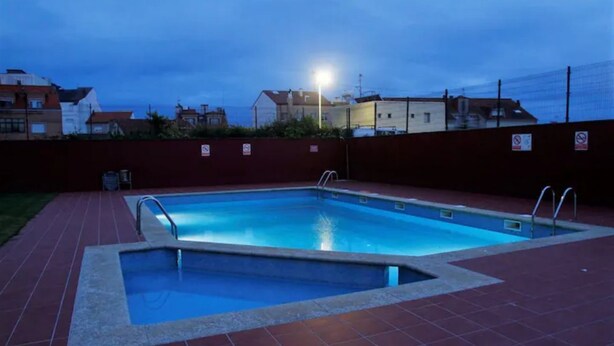 Et rektangulært swimmingpool med fliseterrasse, omgivet af en lav mur og et hegn.
