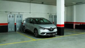 En parkeringskælder med en sølvfarvet bil parkeret i en reserveret boks, hvide søjler og nummererede garageporte.