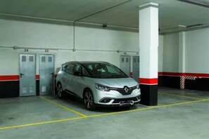 Un garaje con un coche plateado estacionado en un lugar asignado, pilares blancos y puertas de garaje numeradas.