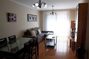 A living room with a glass dining table, a sofa, a coffee table, and two wall-mounted light fixtures.