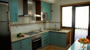 Una cocina con armarios color esmeralda, estufa de acero inoxidable, microondas, pileta y ventana con cortinas.