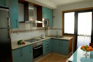 A kitchen with teal cabinets, a stainless steel range, a microwave, a sink, and a window with curtains. - Disconnectaengalicia La Perla Superior, swimming pool and parking (Portonovo)