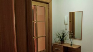 Una puerta de madera con un panel de vidrio, un tocador de madera con un espejo, un teléfono y una planta.