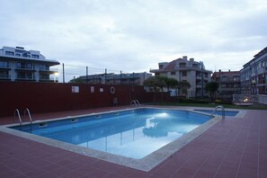 A swimming pool with a red tiled deck, surrounded by buildings.