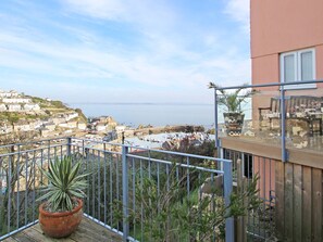A balcony with a potted plant, overlooking a coastal town with buildings and the sea. - Wheal Kendall (St Austell)