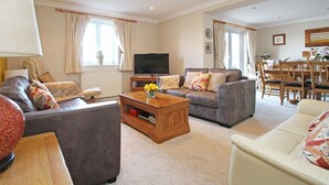 A living room with a sofa, armchair, coffee table, TV, and a dining area with a table and chairs. - Wheal Kendall (St Austell)