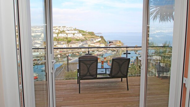 A balcony with two chairs and a table, overlooking a coastal town and the sea. - Wheal Kendall (St Austell)