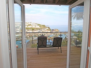 A balcony with two chairs and a table, overlooking a coastal town and the sea. - Wheal Kendall (St Austell)