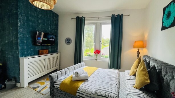A bedroom with a bed, a TV, a window with curtains, a bedside lamp, and a view of greenery outside. - Entire Pet Friendly Apartment- Self Check In/Out (Kelty)