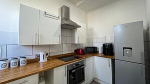 A modern kitchen with white cabinets, a stainless steel range hood, a built-in oven, a microwave, a coffee maker, and a refrigerator. - Entire Pet Friendly Apartment- Self Check In/Out (Kelty)