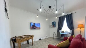 A living room with a foosball table, a red sofa, a television, and a dining area. - Entire Pet Friendly Apartment- Self Check In/Out (Kelty)