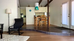Een woonkamer met een zwarte stoel, een wit, pluizig vloerkleed en een eethoek met houten stoelen en een tafel.