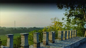A stone balustrade overlooking a green landscape with a power line tower in the distance. - Camping Ground Gunung Mijil Hils (Bantul)