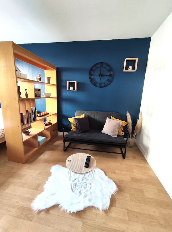 A living room with a blue wall, a dark sofa, a wooden bookshelf, a round coffee table, and a white furry rug.