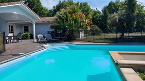 A swimming pool with a wooden deck, lounge chairs, and a house with a tiled roof. - Large villa, swimming pool, wooded garden, close to lakes and ocean. Ideal for families. (Pontenx-les-Forges)