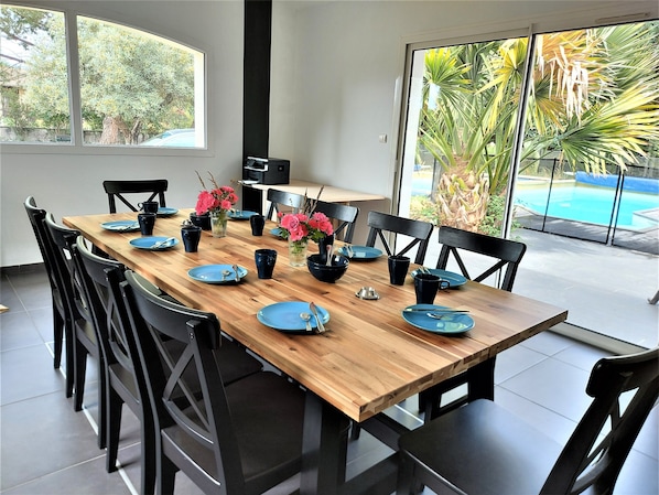 A dining area with a wooden table set for six, black chairs, and a view of a swimming pool through large windows.