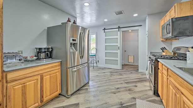 Une cuisine moderne avec des meubles en bois, des appareils en acier inoxydable et un parquet en bois disposé en chevrons.