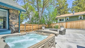 Un jardin avec un jacuzzi, un mur en pierre, une clôture en bois et une maison dotée d’une cheminée.