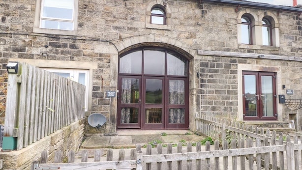 A stone building with a large arched window, a wooden fence, and a sign that reads "The Mistal." - Bronte Barn (Keighley)