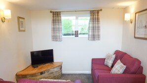 A living room with a flat-screen TV on a wooden stand, a red sofa, and a matching armchair. - Bronte Barn (Keighley)