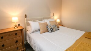 A neatly made bed with white bedding and multiple pillows, flanked by wooden nightstands with lamps. - Bronte Barn (Keighley)