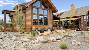 A modern log cabin with large windows, a stone chimney, and a patio area with outdoor seating. - Elk Haven! Private Jacuzzi, Indoor/Outdoor Fireplace, Two Large Patios (Estes Park)