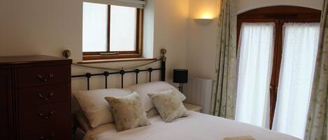 A bedroom with a bed, a dresser, a nightstand, a lamp, and a window with curtains.