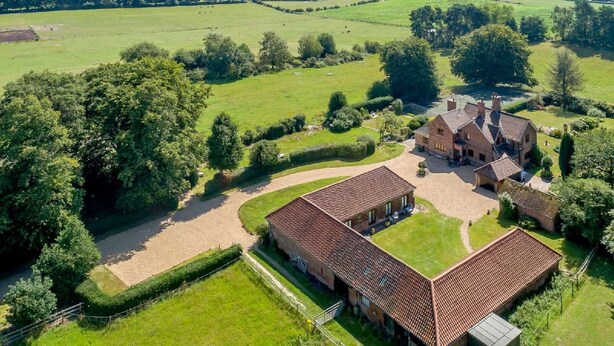 Une vue aérienne d’un vaste domaine comprenant plusieurs bâtiments, de vastes champs verdoyants et un jardin bien entretenu.